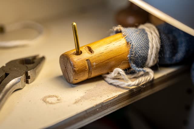 Tight readable process crop inside a public puppet-theater repair closet after rain; one small worn wooden puppet wrist