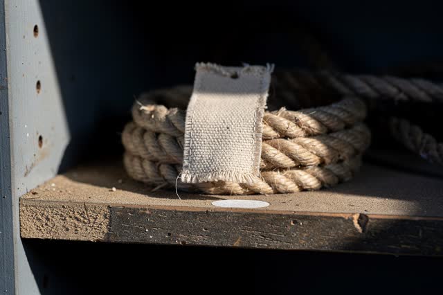 Restful low horizontal crop inside a theater rope-locker cubby after rain; one blank raw-canvas rope tag rests on a coil