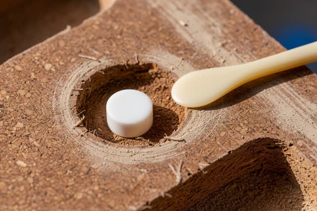 Extreme macro readable process crop inside a public fountain spacer tray after rain; one small off-white porcelain space