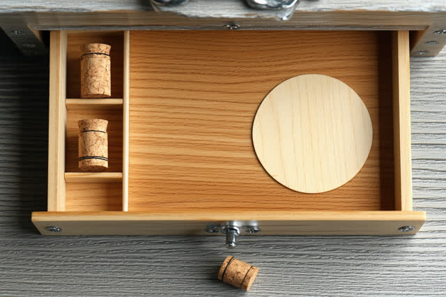 Restful low horizontal crop of a harbor sample cabinet drawer after rain; one plain cork stopper rests in a shallow dry