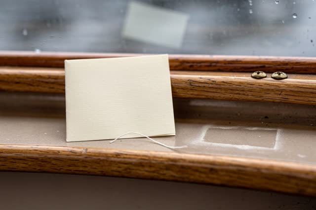 Restful low horizontal crop on a covered ferry reading ledge after rain; one folded blank cream timetable card with no p