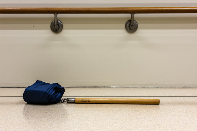 Readable bench-height close crop under a ferry waiting-room umbrella rail after rain; one bent dull-nickel umbrella catc
