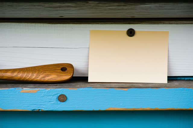 Restful low horizontal crop on a small boathouse harbor-notice shelf after rain; one blank cream harbor slip with no pri