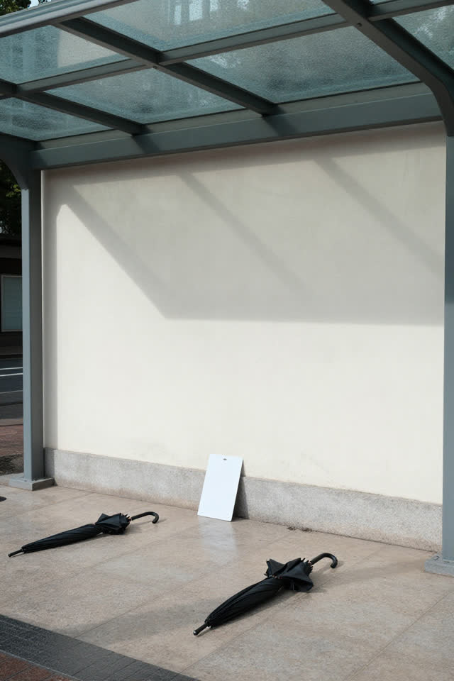 Medium-wide crop of a transit umbrella alcove after rain, dry beneath a glass canopy; several empty umbrella-shaped shad