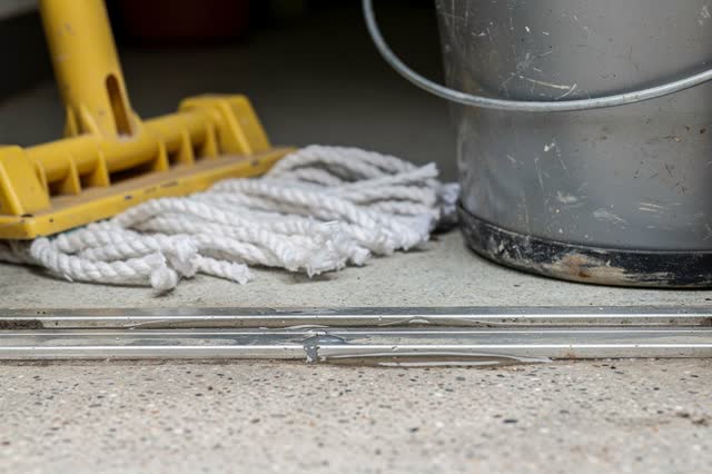 Low close crop at the threshold of a public utility closet after rain. A muted yellow mop wringer handle rests folded do