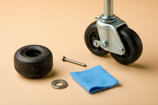 Near-macro low crop under a public library book cart after rain, focused on a scuffed black rubber caster wheel being co