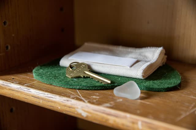 A small key shelf inside a community room cupboard in gentle late-afternoon light. One spare brass key rests on a soft g