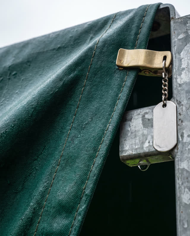 A narrow market-side awning frame after rain, seen in an asymmetrical close-up. Wet canvas pulls diagonally against one