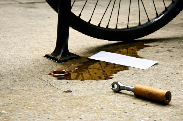 A covered civic bicycle shelter after rain, shown from a low close floor-level view. A loose public bike rack foot is be