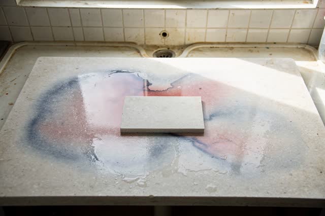 A small community printmaking rinse area after cleanup. An empty pale stone rinse slab holds faint diluted indigo and ro