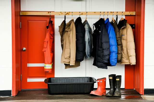 A small volunteer firehouse drying bay in late amber side light. A wall-mounted drying rack is being re-pinned where one