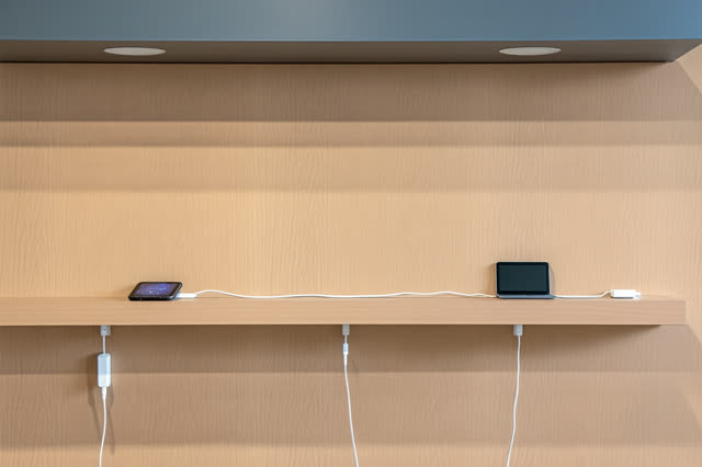 A small public device-charging shelf after the equipment has been put away. On pale wood, a dust-free outline remains wh