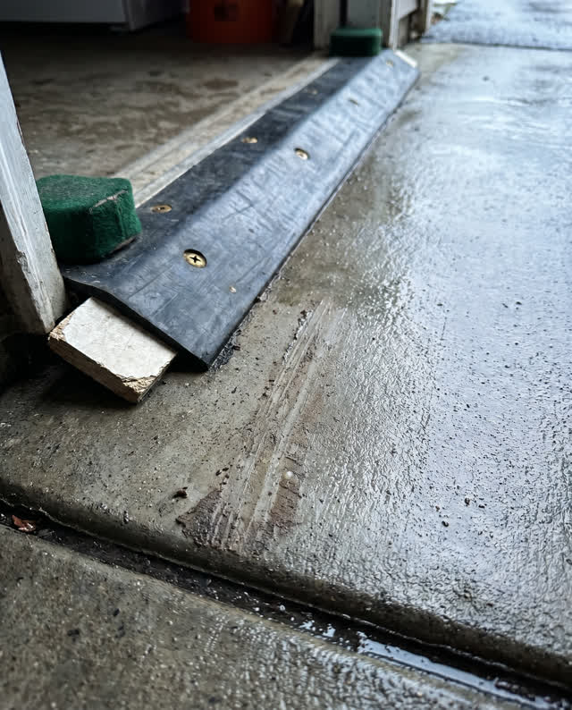 A side entrance to a public instrument repair room after rain, cropped low and empty of people. One charcoal rubber thre