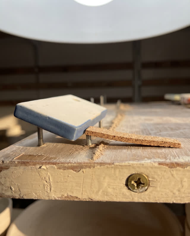 A ceramics glaze-test shelf after humid air softened one spacer, empty of people, with no readable labels, seed drawer,