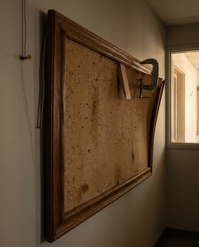 A quiet community hallway corner with an empty cork notice board after humid weather, empty of people, with no paper on