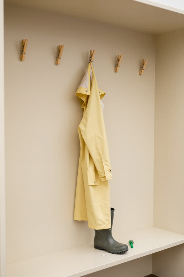 A small community cloak alcove after a dry morning, empty of people, with no question marks, readable labels, signage, s