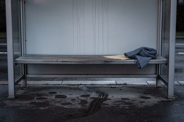 A covered public tram-stop bench alcove after light rain, empty of people, with no readable transit signs, labels, adver