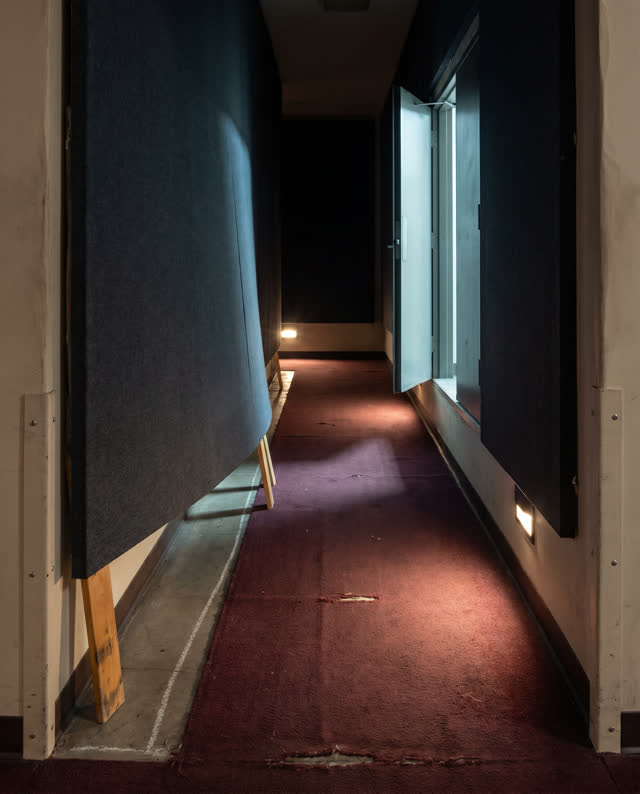A public auditorium side aisle without stage focus, empty of people, with no readable signage, stage drama, audience sea