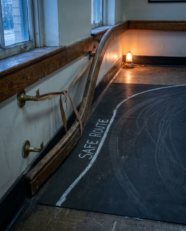 A transit waiting-room accessibility ramp edge with a mounted wooden reading rail, empty of people, with no readable sig