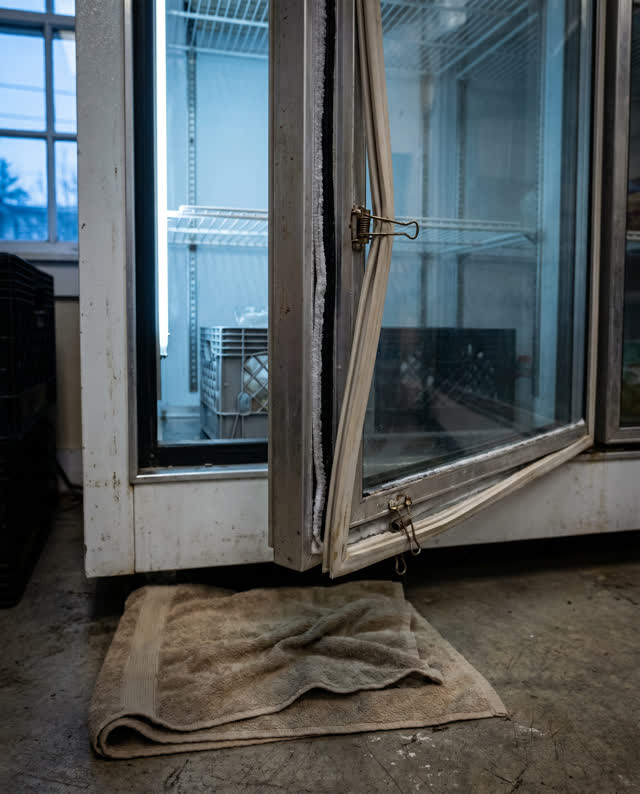 A community pantry freezer corner with one small maintenance light on, empty of people, with no readable labels, storage