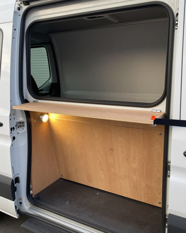 A mobile civic outreach van interior with a fold-out service counter beneath a side window, empty of people, with no rea
