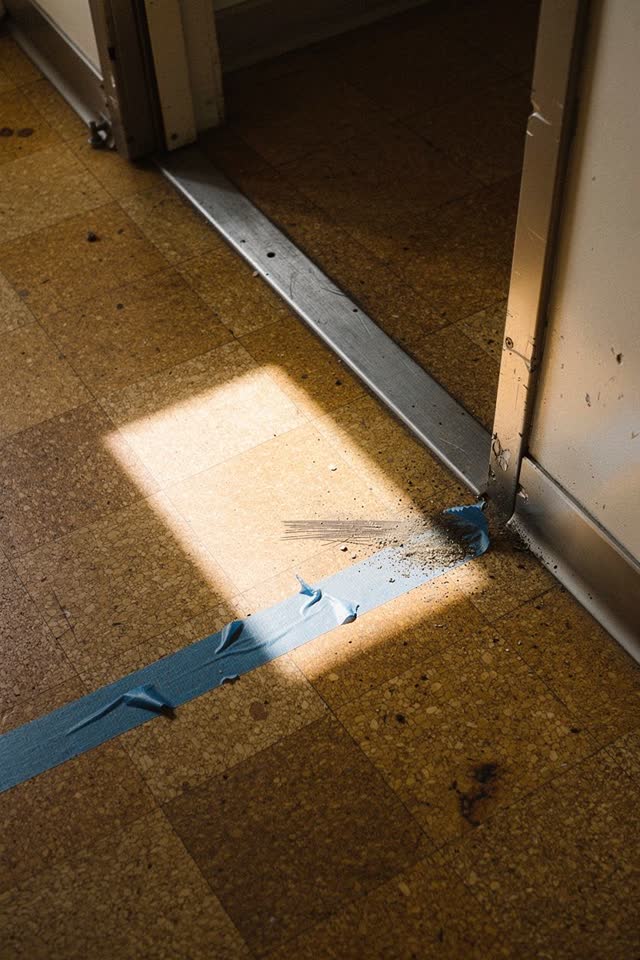 A small public craft-room side corridor with cork tile flooring, empty of people, with no readable text, corkboard pins,
