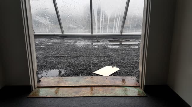 A civic roof-access vestibule opening onto a post-rain roof, seen from inside, empty of people, with no readable text, p