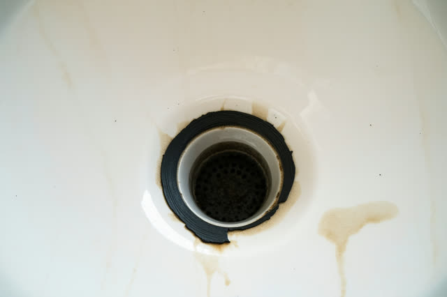 A community darkroom wash sink with the safelight off and daylight leaking through a high frosted window, empty of peopl