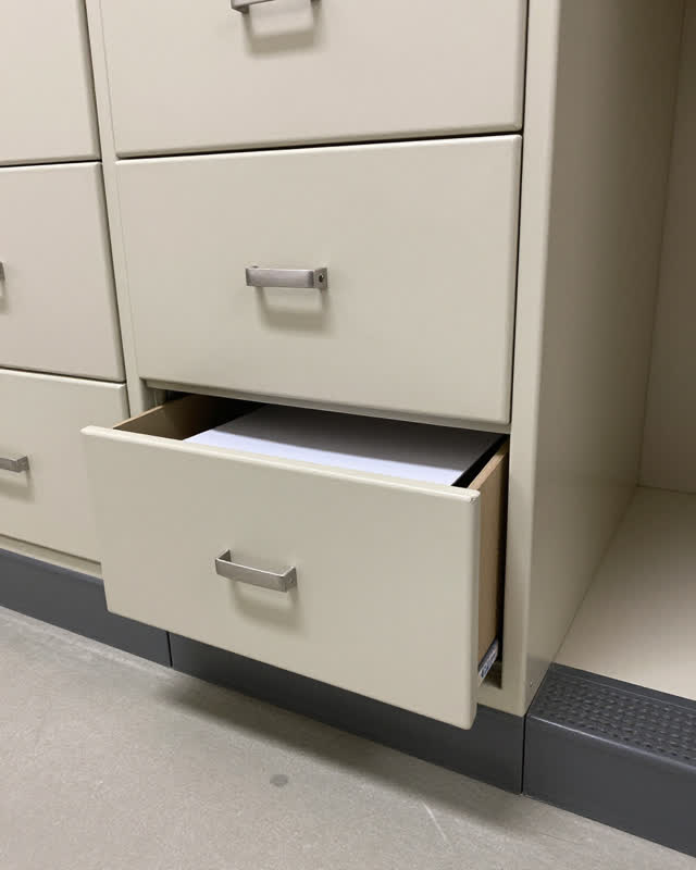 A public copy-room side cabinet after supplies were checked, empty of people, with no readable labels, door sweep repeti