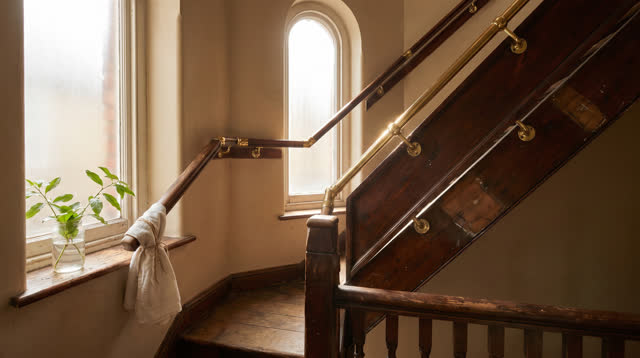 An inviting dream in an old stair landing: repaired dark-wood handrails climb diagonally from lower left to upper right,