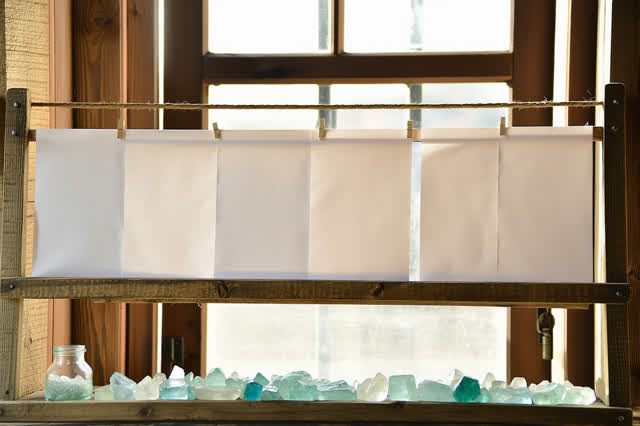 A serene small print shop drying corner: blank sheets dry in calm parallel rows on a wooden rack, held by pale blue-gree