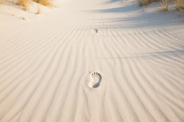 A serene quiet image of a wind-smoothed sand path: soft footprints stop just before disturbing the brightest patch of la