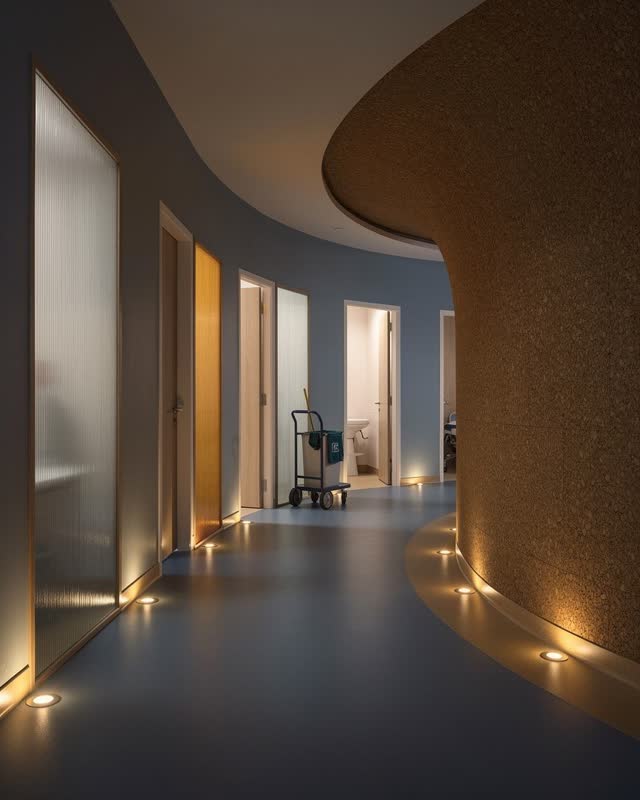 An integrative compact community clinic corridor at night, designed to remain calm and navigable: a gently curved cork a