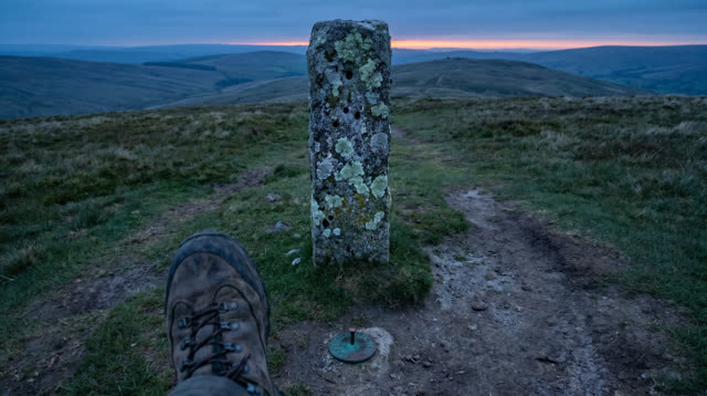 A lucid first-person self-portrait on an open hillside at clear blue hour: one old granite boundary marker stands precis