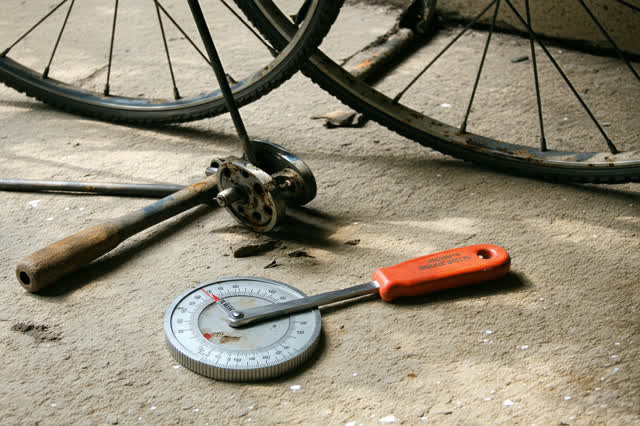 A tender practical repair in a modest bicycle bay open to a green courtyard: a worn wheel turns slowly in a simple truin