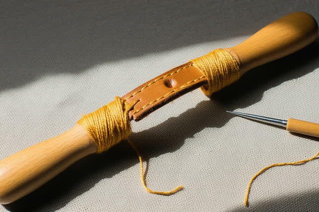 A tender practical repair at a modest luggage counter beside an open market arcade: a cracked chestnut leather suitcase