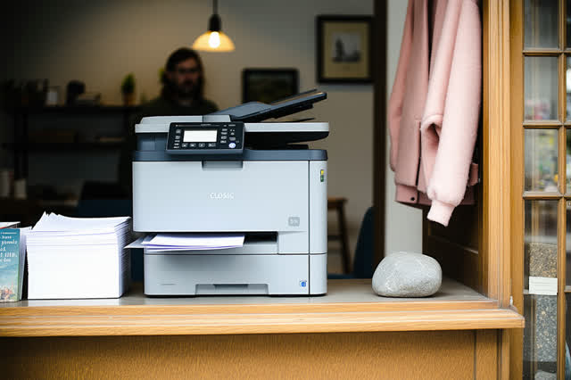 A genuinely quiet image in a small neighborhood copy shop after closing. One matte graphite copier stands stopped and co