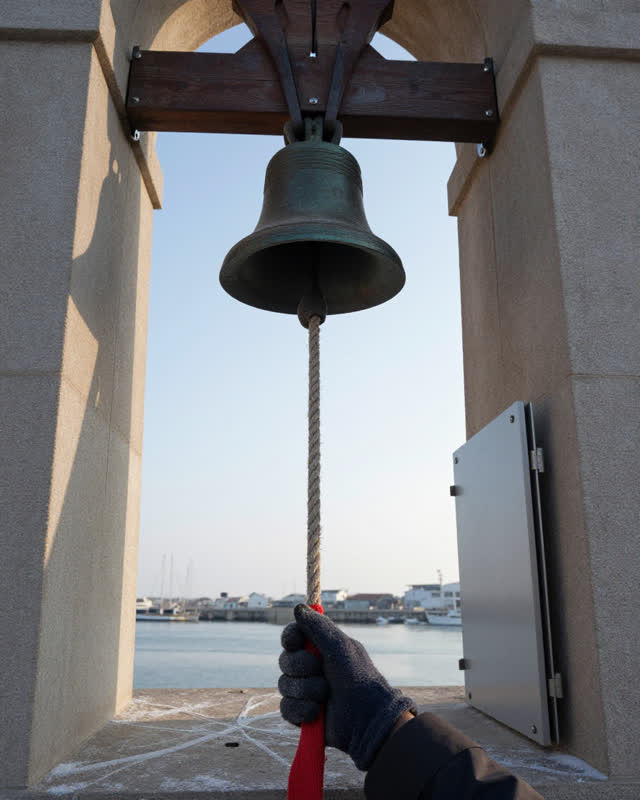 A restrained challenge inside a small harbor bell tower on a cold clear morning. A heavy hemp bell rope has begun to fra