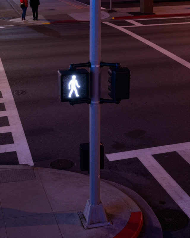 A restrained low-tension challenge at a quiet downtown intersection late at night. A pedestrian countdown display operat