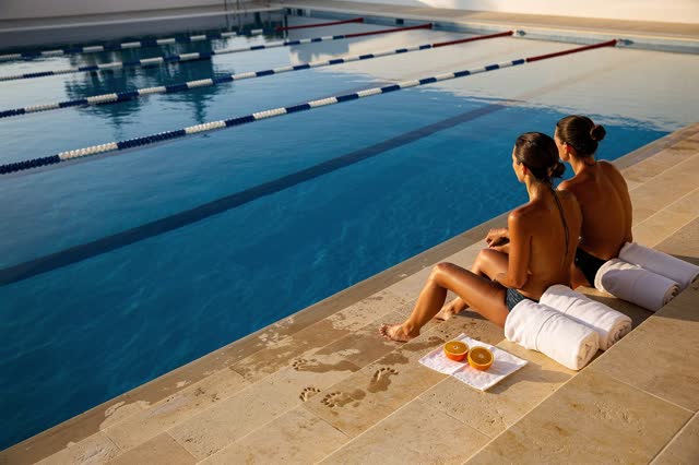 A genuinely quiet image on broad limestone steps beside an outdoor swimming pool after the morning session. Two swimmers
