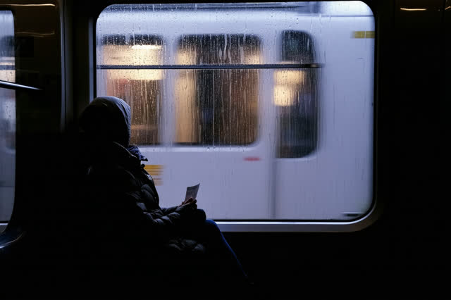 A genuinely quiet image inside a nearly empty tram moving through a rainy city at night. One passenger sits comfortably
