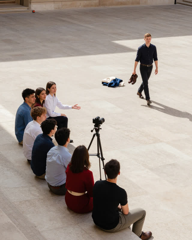 A precise medium-tension scene in a sunlit courtyard during an informal group portrait. Eight friends sit and stand natu