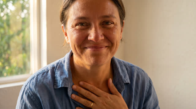 A close lucid portrait in a plain room beside an open late-afternoon window. One adult faces the camera immediately afte