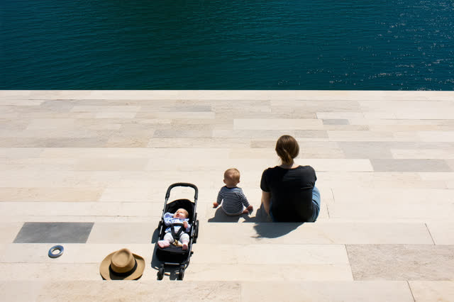 A genuinely quiet open harbor landing between ferry departures. One adult sits comfortably on a broad sun-warmed limesto