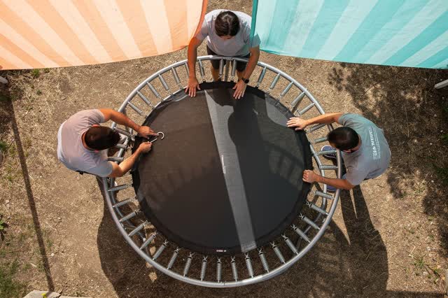 A cheerful practical repair viewed from directly overhead in a shaded backyard recreation area. Three adults are spaced