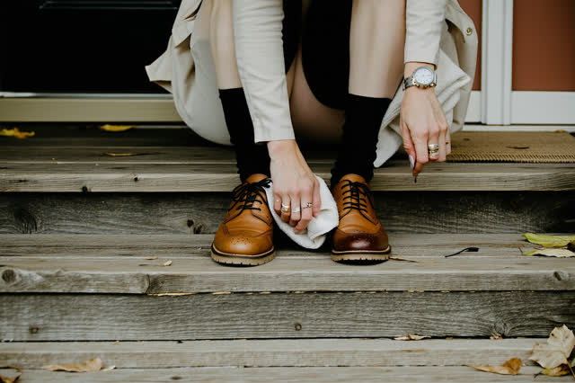 A genuinely quiet back porch during steady afternoon rain. One adult sits naturally on a low wooden step, slowly polishi