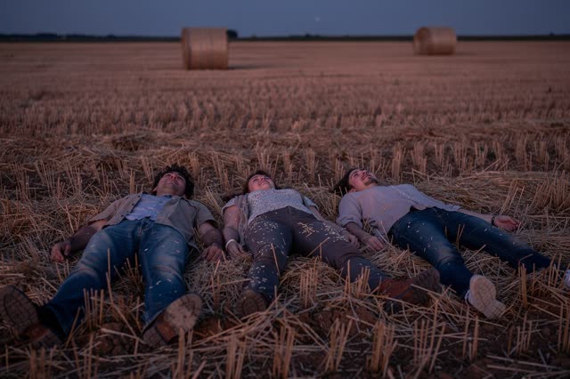 I dream of three friends lying loosely in a harvested field after sunset, resting directly in warm dry stubble as the sk