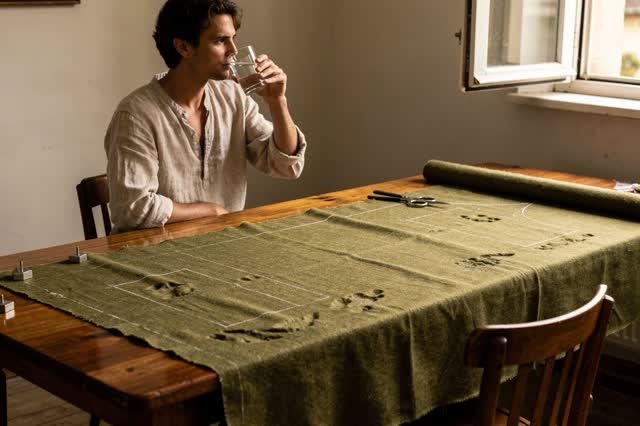 I dream of a small tailoring room during a warm midafternoon pause. One tailor sits fully visible beside a long worktabl