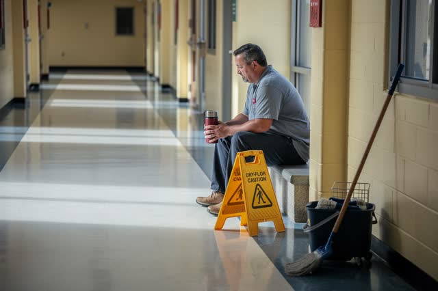 I dream of a school corridor after floor maintenance, quiet and safe before anyone returns. One adult custodian sits off