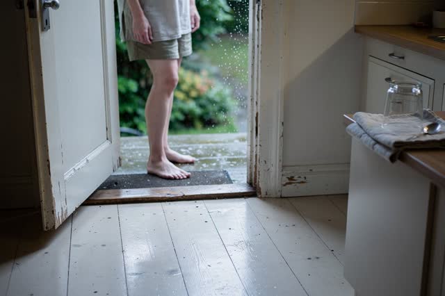 I dream of a plain domestic threshold between a kitchen and a back step after rain. One person stands barefoot at the op